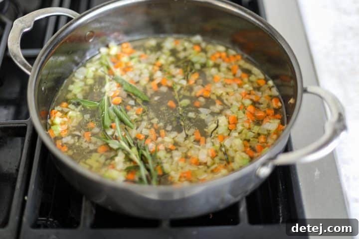 Broth being added to sautéed mirepoix in a pan, deglazing the bottom.
