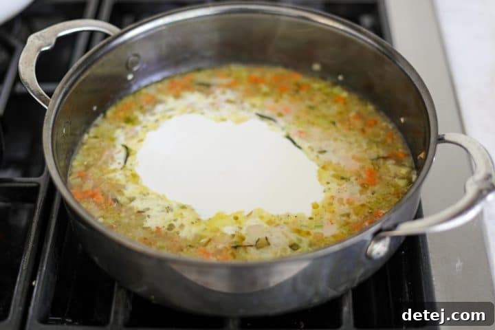 Heavy cream being poured into the vegetable and broth mixture, forming a creamy sauce base.