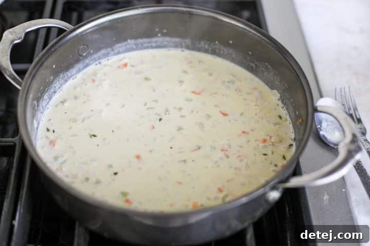 Cooked chicken cutlets being nestled back into the rich, creamy sauce with vegetables.