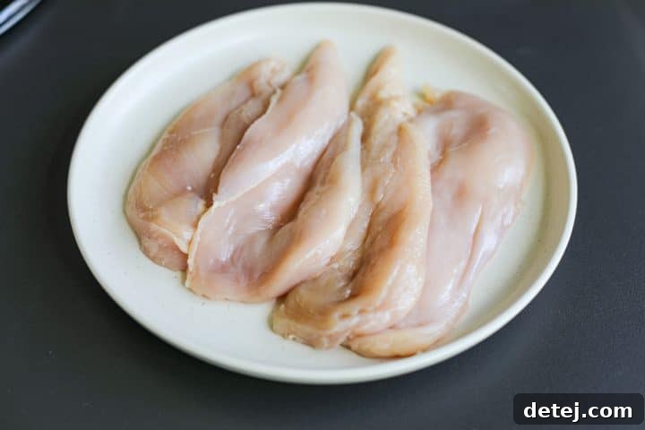 Two chicken breasts butterflied and laid flat on a plate, ready for seasoning.