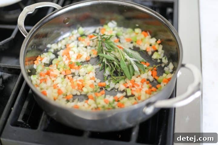 Mirepoix sautéing in a pan with fresh sprigs of thyme, rosemary, and sage.