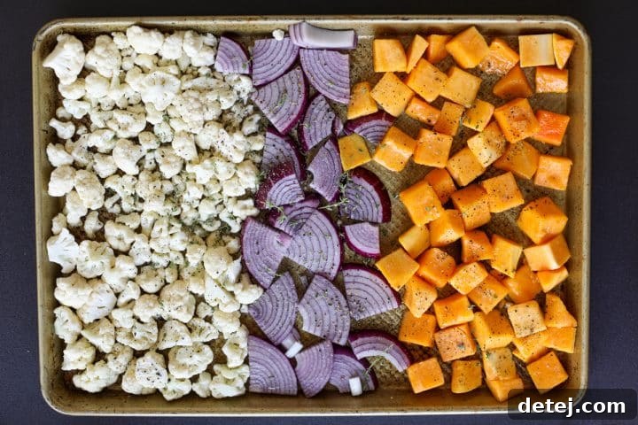 Cubed butternut squash, cauliflower florets, and sliced red onion spread on a baking tray, seasoned and ready for the oven.