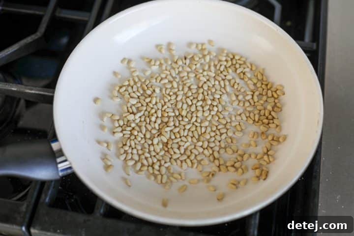 Pine nuts being toasted in a nonstick pan over medium heat until golden brown.