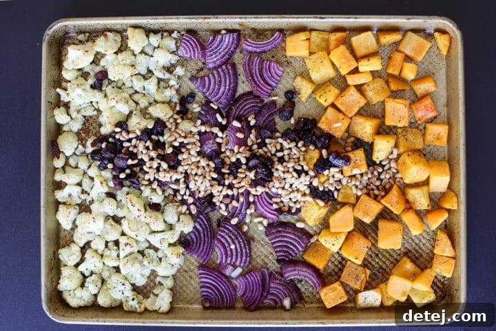 Roasted butternut squash, cauliflower, and red onion on a sheet tray with toasted pine nuts and dried cranberries added.