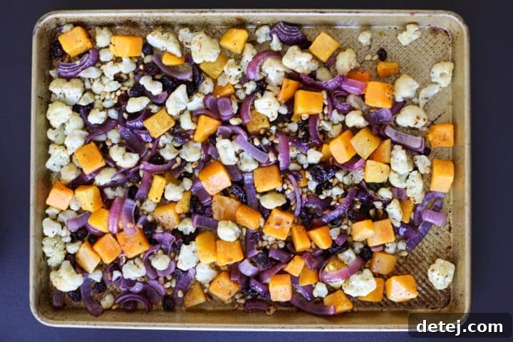 All roasted ingredients, including squash, cauliflower, red onion, pine nuts, and cranberries, tossed together on a sheet tray.
