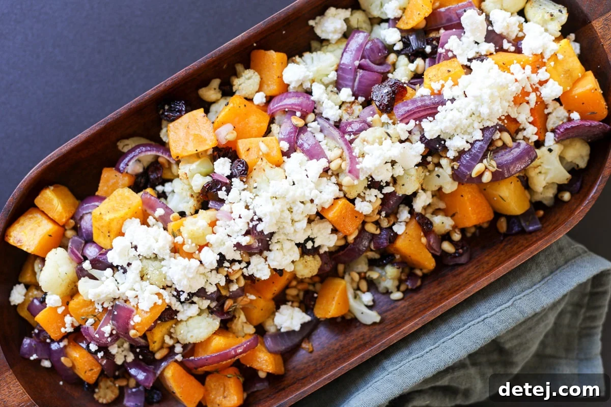 Close-up of the finished Roasted Butternut Squash, Cauliflower and Red Onion dish in a rustic bowl, garnished with fresh herbs and crumbled goat cheese.