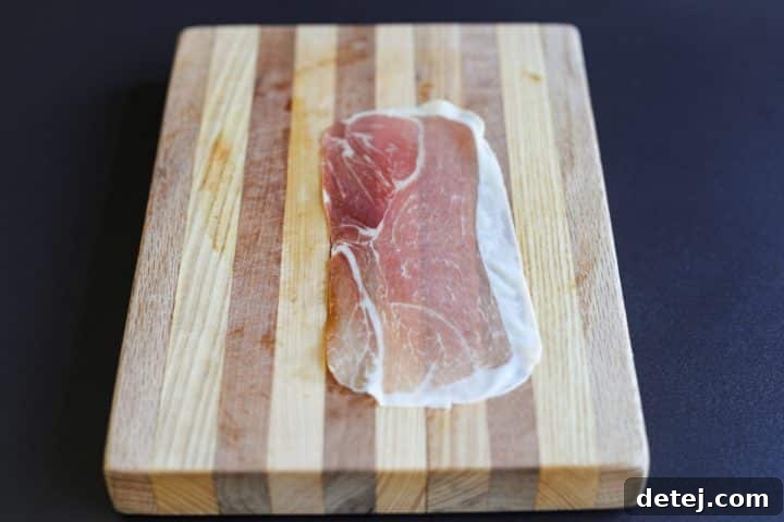 A single slice of prosciutto laid flat on a cutting board, ready for filling.