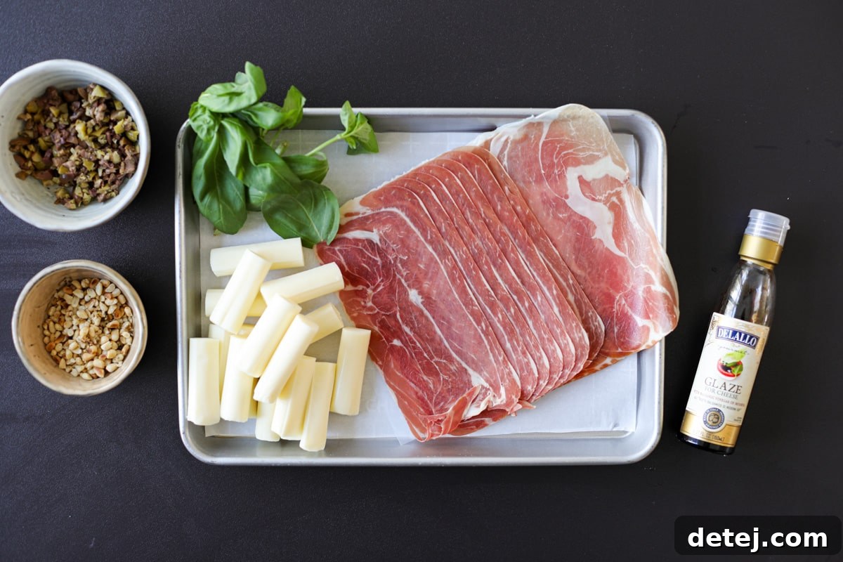 Ingredients laid out for Crispy Prosciutto and Mozzarella Roll-Ups, including prosciutto, mozzarella sticks, olives, basil, balsamic glaze, and pine nuts.