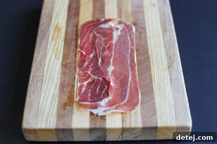 A single slice of prosciutto laid flat on a cutting board, ready for filling.