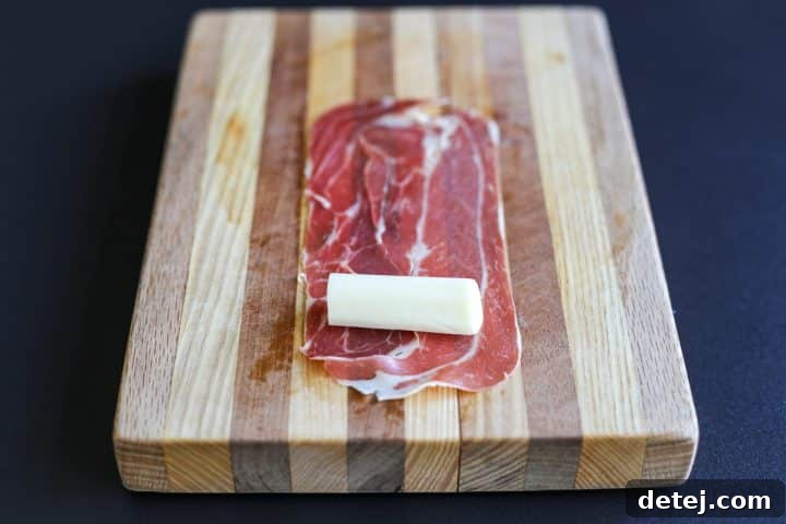 Prosciutto slice with a piece of mozzarella cheese placed at one end.
