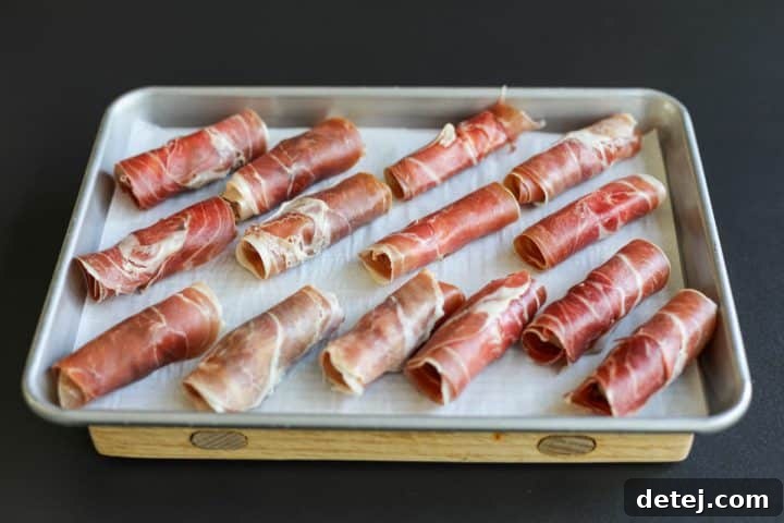 Prosciutto, mozzarella, and olives rolled up into a neat cylinder, on a tray.