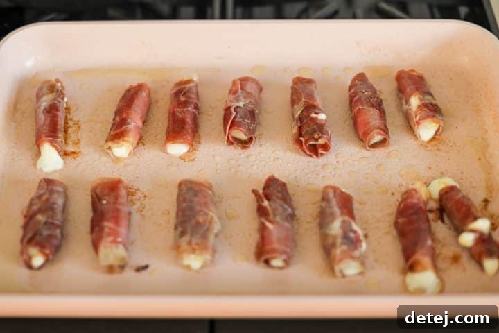 Several prosciutto roll-ups searing in a hot nonstick pan, developing a crispy crust.