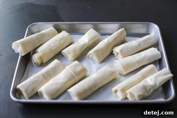 Brie and date roll-ups neatly arranged on a parchment-lined baking tray, ready for cooking