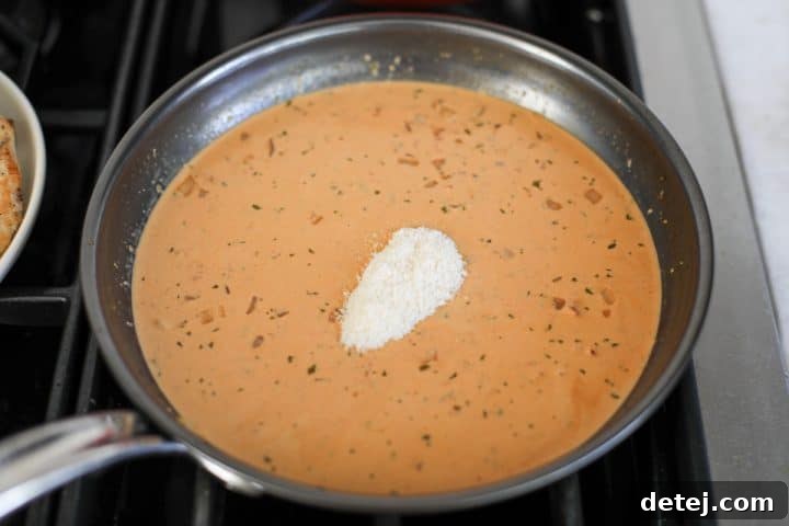 Freshly grated Parmesan cheese melting into the creamy sun-dried tomato pesto sauce in the pan.