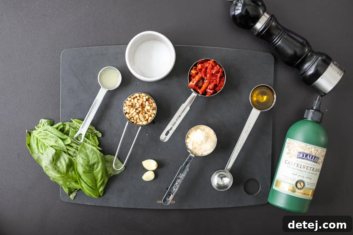 Assorted fresh ingredients for homemade sun-dried tomato pesto including basil leaves, pine nuts, Parmesan cheese, and sun-dried tomatoes.