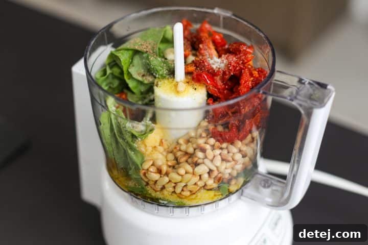 Ingredients for homemade sun-dried tomato pesto inside a mini food chopper, ready for blending.
