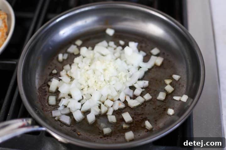 Finely diced yellow onions and minced garlic sautéing in the same pan, inheriting the chicken's fond.
