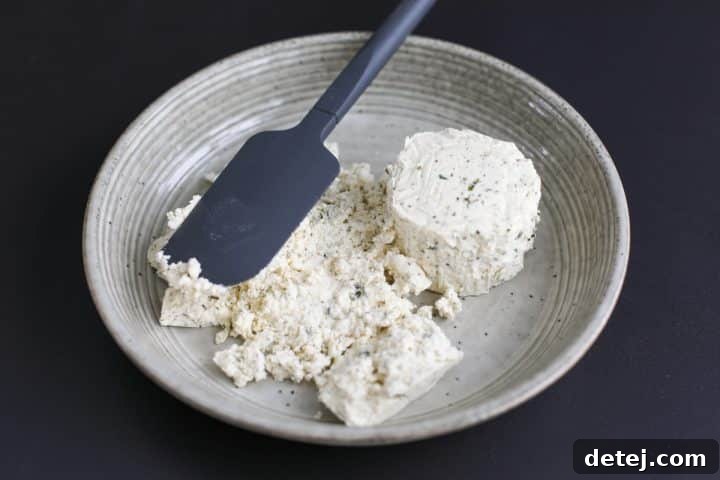 Two blocks of Boursin cheese being gently pressed and spread into the bottom of a serving bowl.