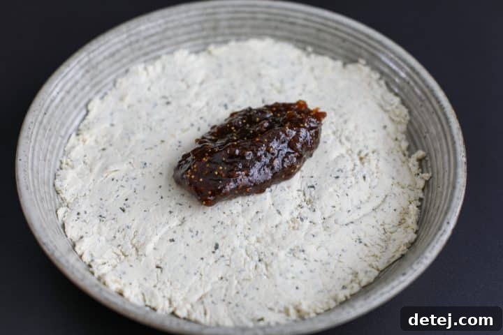 A spoonful of fig jam being added directly on top of the spread Boursin cheese layer in the bowl.