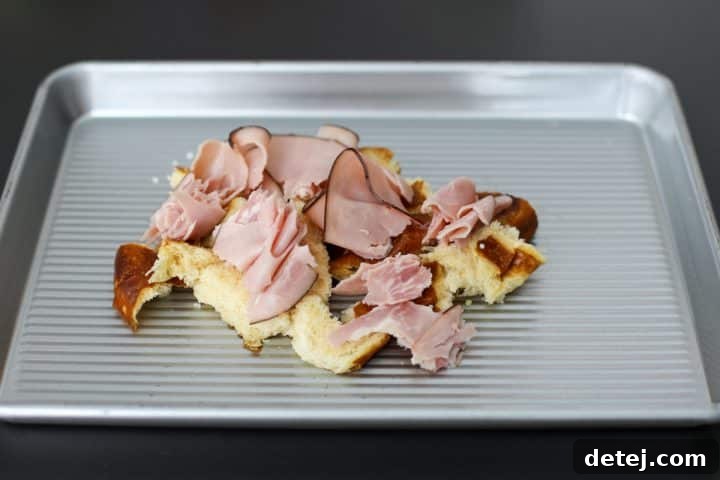 Black forest ham added to the torn pretzel roll on a baking tray.