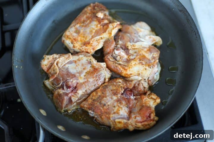 chicken thighs searing in a hot nonstick pan.