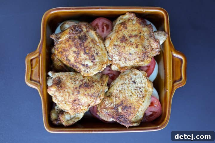 seared chicken thighs arranged in a ceramic baking dish with vegetables.