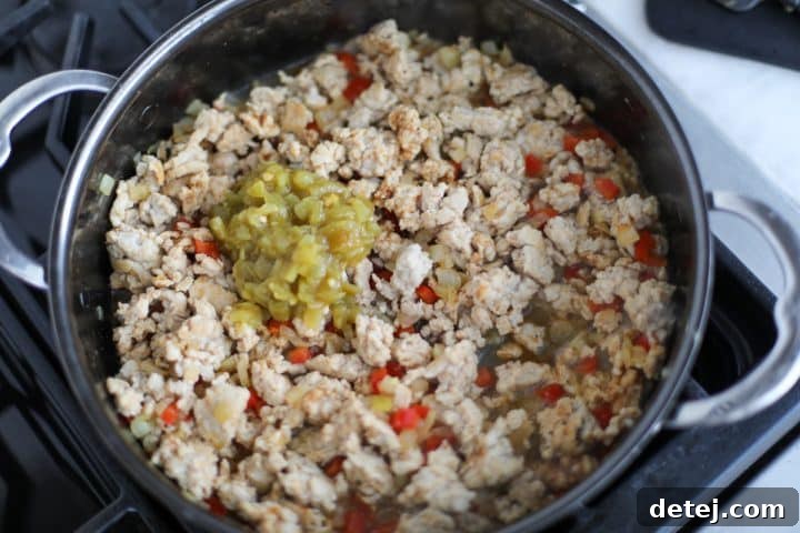 low sodium chicken broth and diced green chilies in a pan with ground chicken mixture.