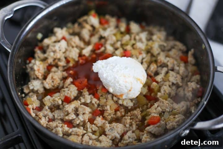 taco sauce and whipped cream cheese in a pan with ground chicken.