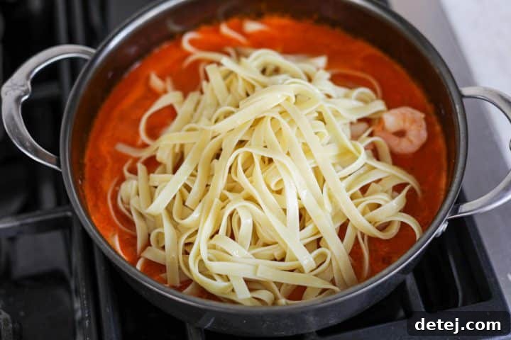 Smoky Red Pepper Shrimp Pasta 13 Cooked shrimp and al dente pasta being tossed into the creamy roasted red pepper sauce in a pan.