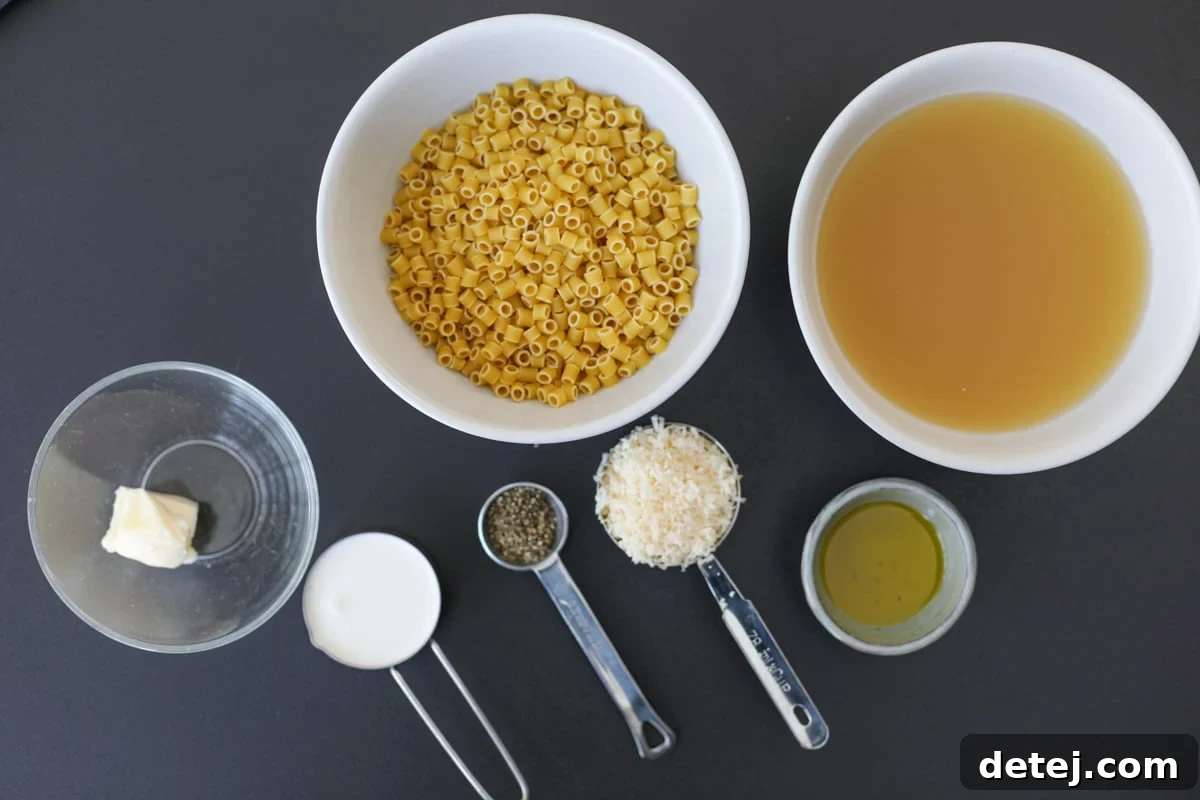 All essential ingredients for the creamy cacio e pepe pasta recipe laid out: ditalini pasta, olive oil, cracked black pepper, chicken broth, heavy cream, butter, and freshly grated parmesan cheese.