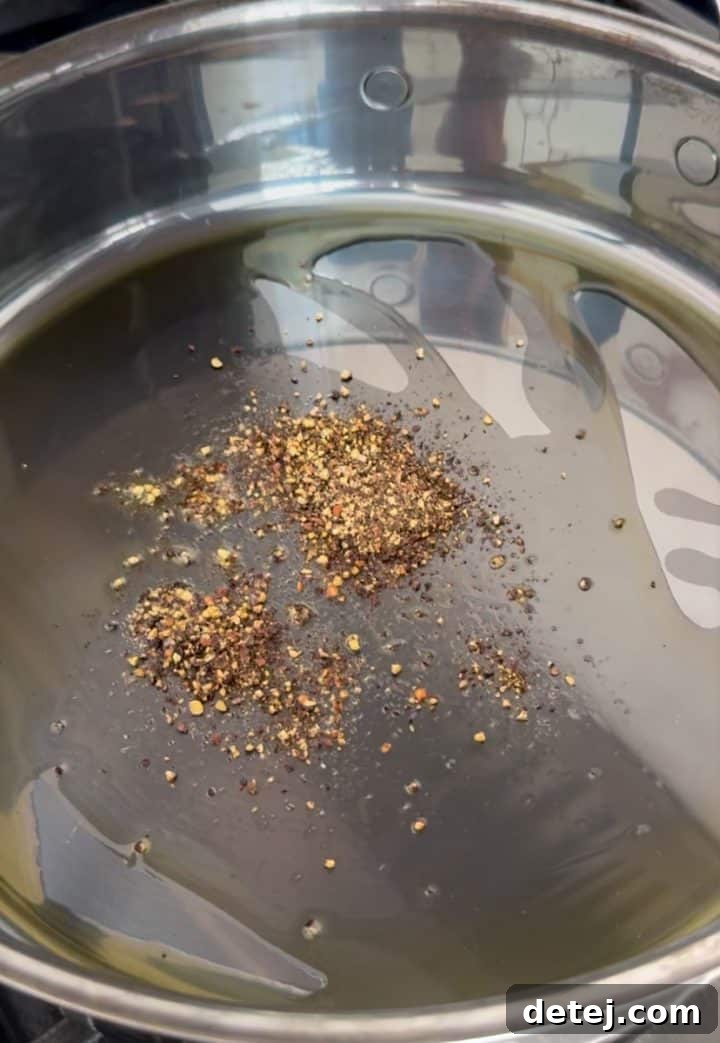 Cracked black pepper being bloomed in a pan with olive oil, releasing its fragrant aroma.