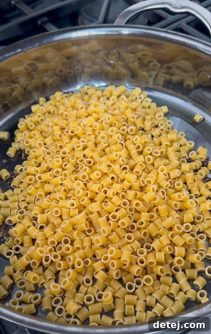 Ditalini pasta being sautéed in a pan with the bloomed pepper and olive oil.