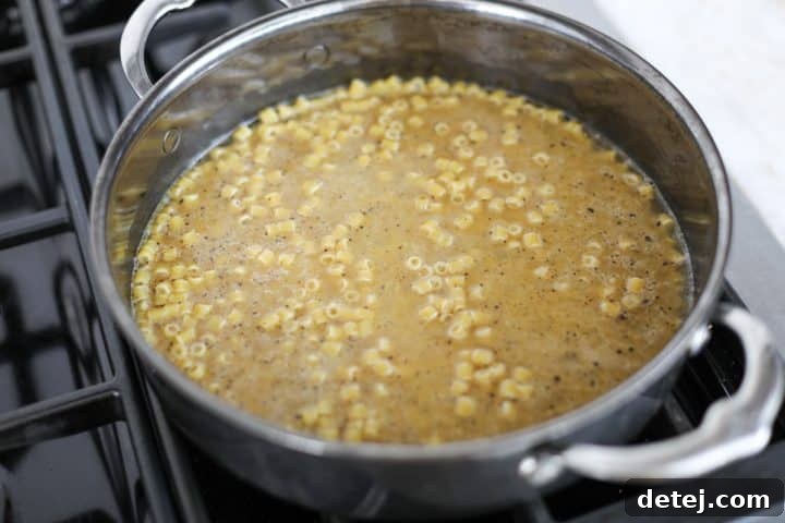 Chicken broth being poured into the pan with ditalini pasta and pepper, ready to simmer.