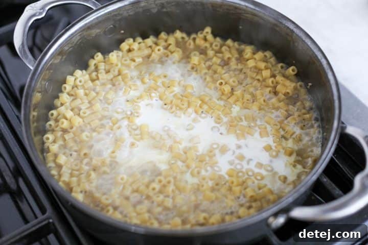 Heavy cream being stirred into the pasta and sauce mixture, enhancing creaminess.