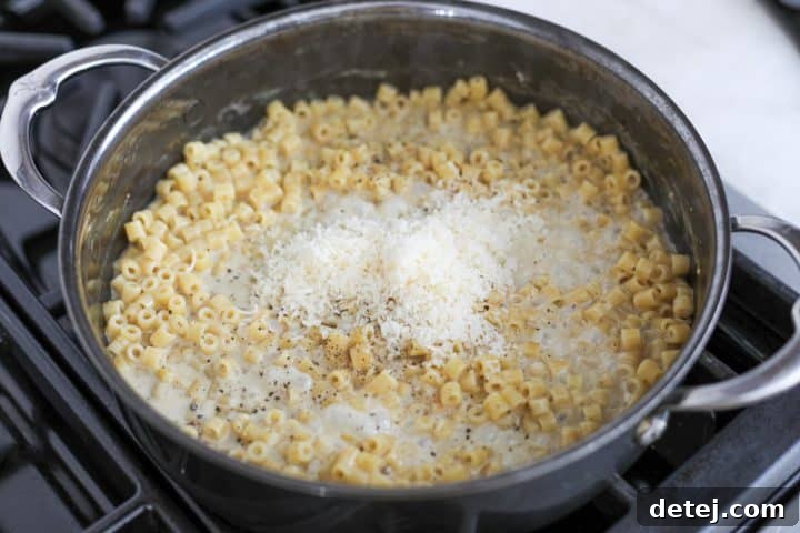 Freshly grated parmesan cheese being folded into the hot, creamy ditalini pasta sauce.