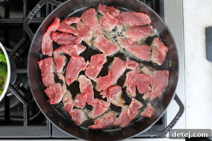 Thinly sliced beef searing in a hot pan in a single layer.