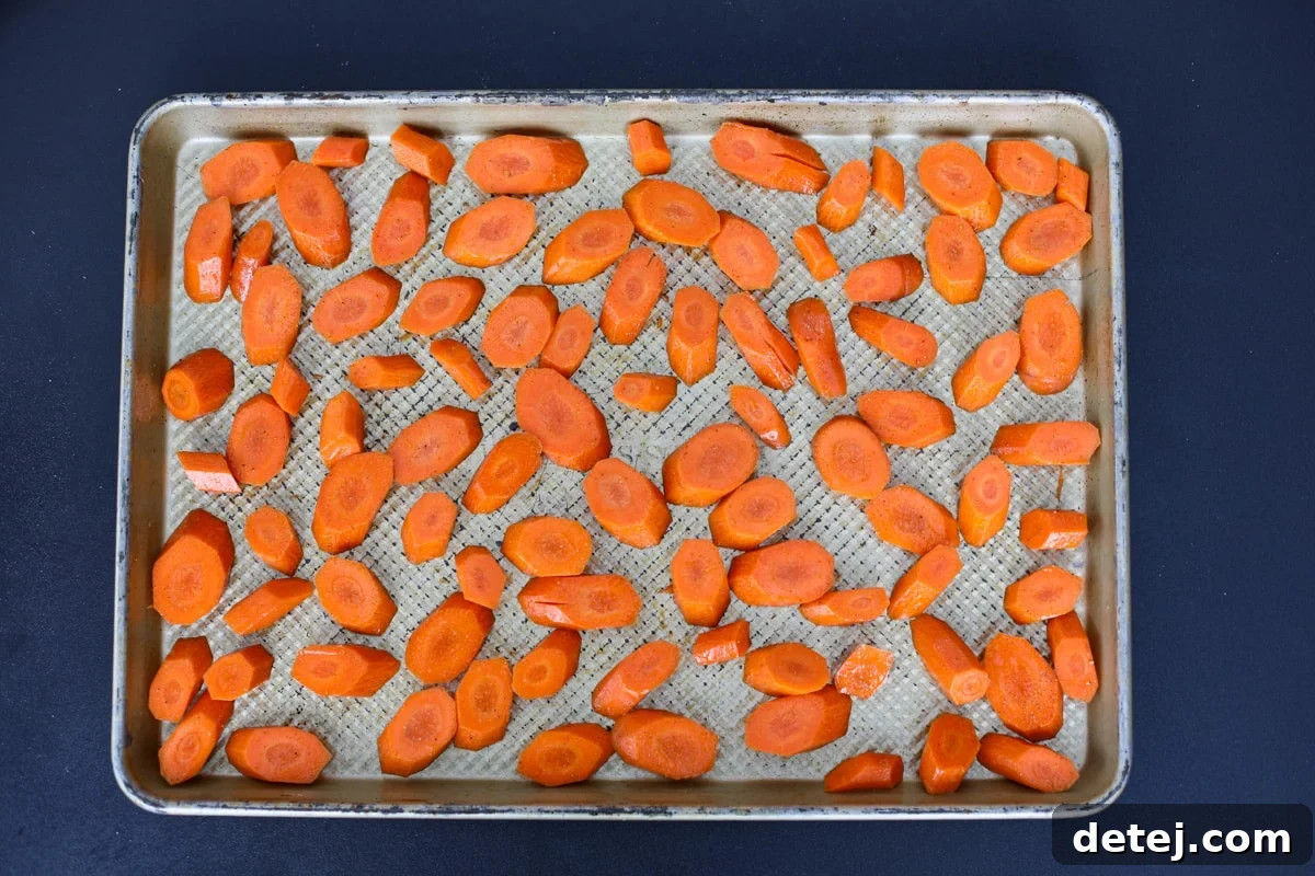 Seasoned carrots spread in a single layer on a baking tray.