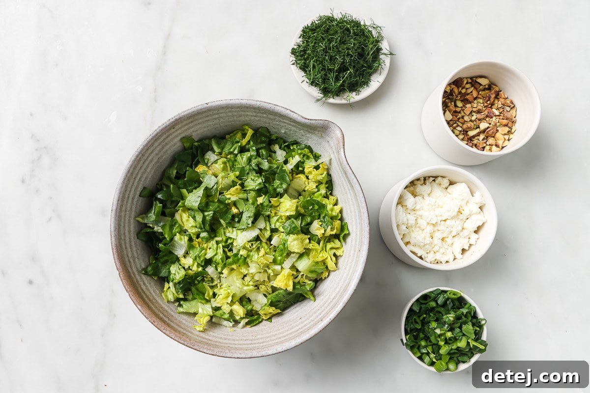 A collection of fresh ingredients laid out, ready for preparation of the Chopped Greek Salad, including lettuce, onions, dill, and feta cheese.