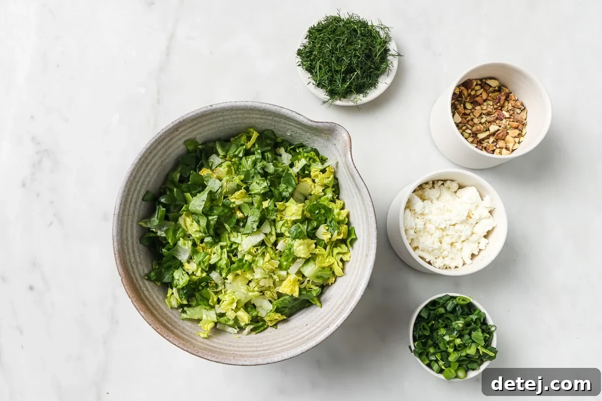 A colorful array of fresh ingredients for Greek Salad with Dressing laid out on a wooden board, including romaine lettuce, green onions, fresh dill, feta cheese, and pistachios.