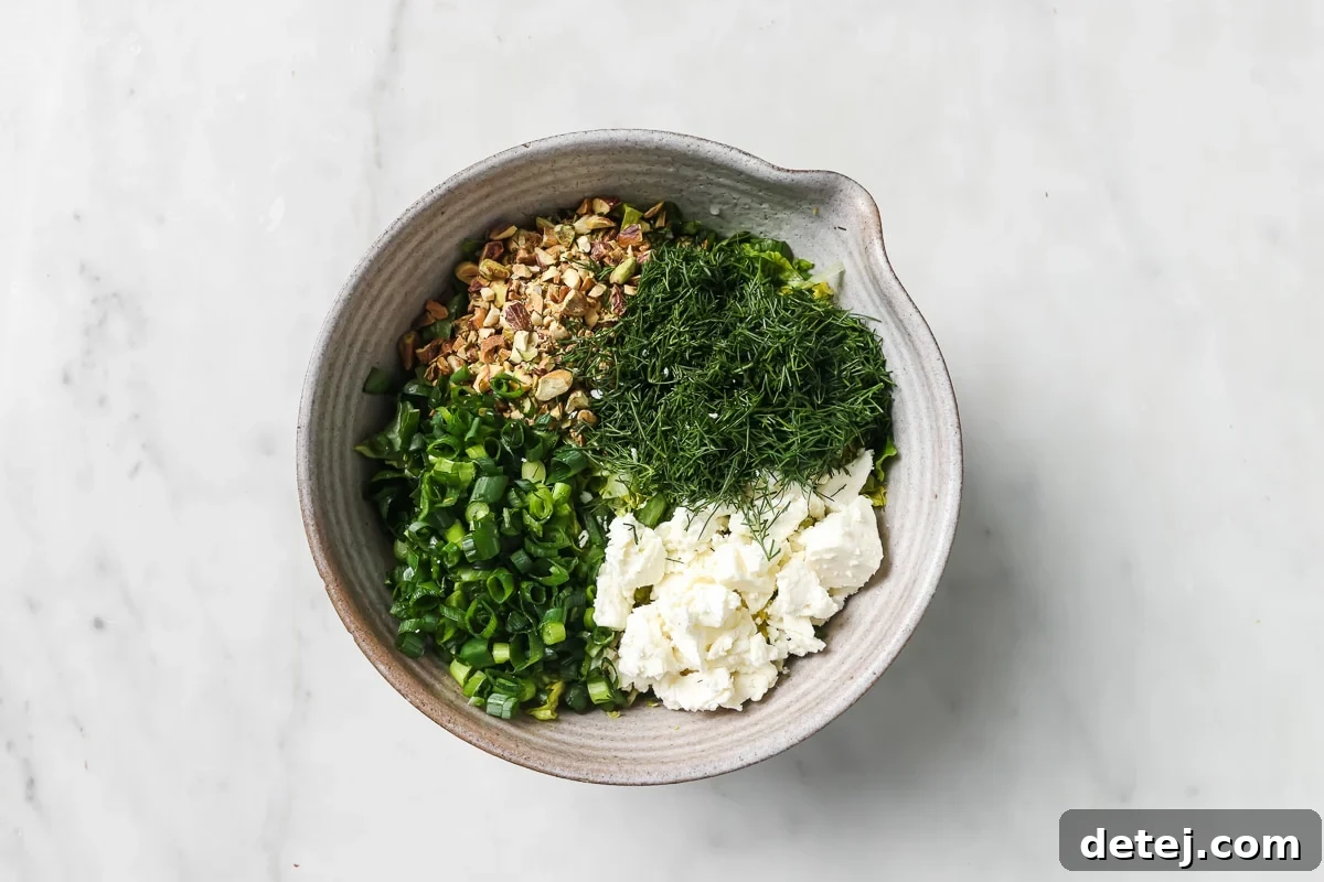 A large mixing bowl containing all the chopped salad ingredients before dressing, including romaine, green onions, dill, feta, and pistachios.