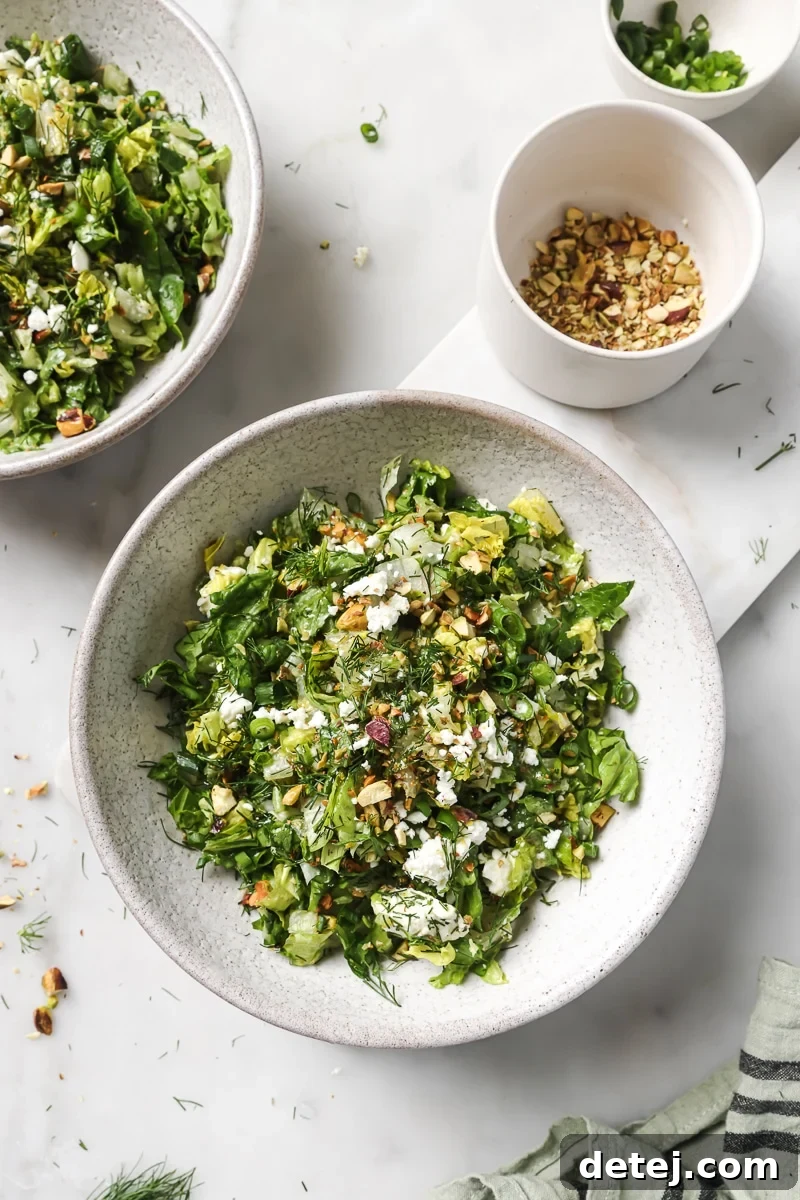 A close-up shot of the finished Chopped Greek Salad, featuring crisp greens, crumbled feta, green onions, and pistachios, perfectly dressed and ready to eat.