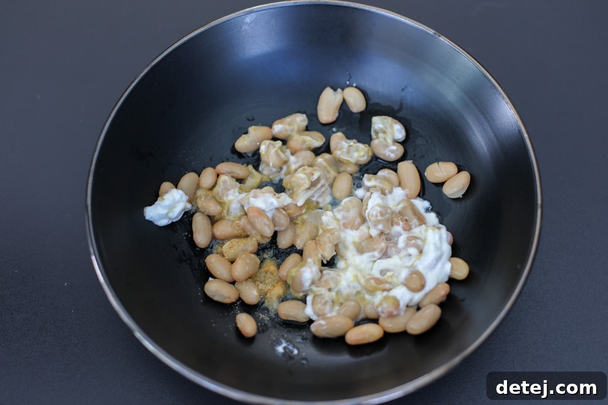 Great northern beans and creamy dressing being mixed in a bowl.