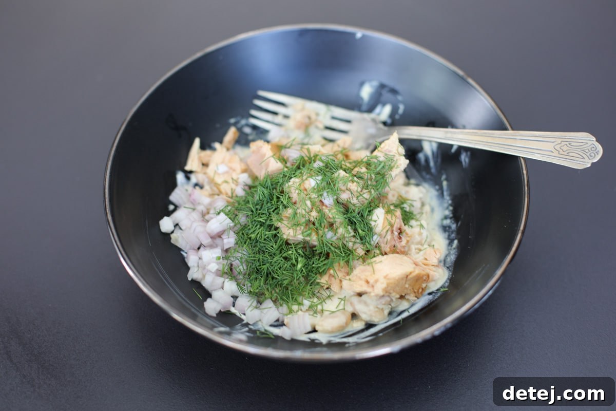 Tuna, beans, shallots, and fresh dill combined with the creamy dressing in a mixing bowl.