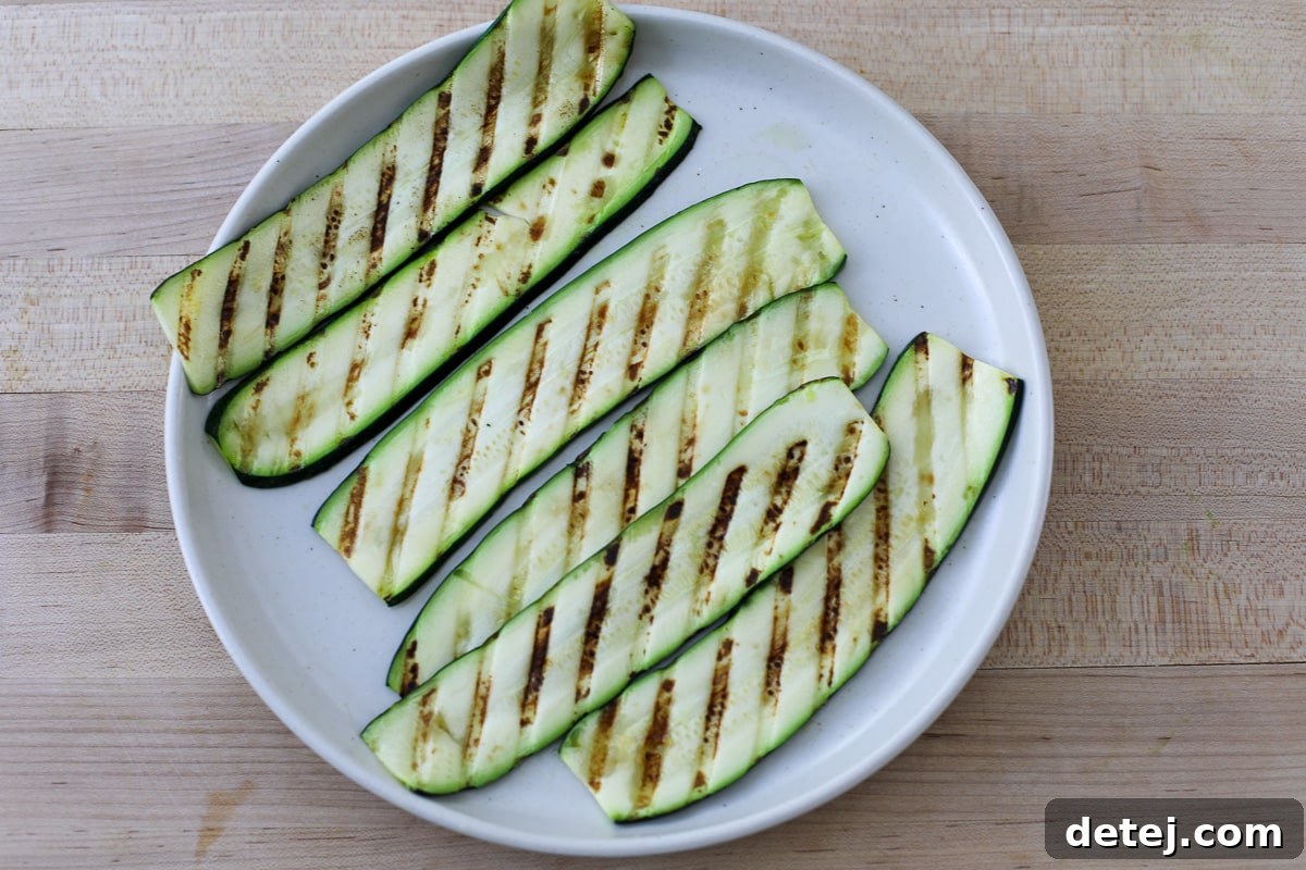 Grilled zucchini slices arranged neatly on a grill pan, showing distinct char marks.