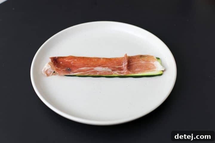 A slice of prosciutto being placed over a grilled zucchini slice.