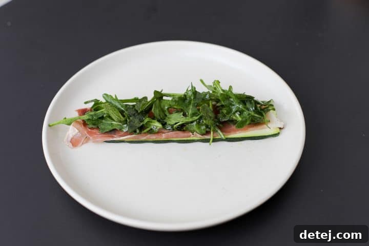 Lightly dressed arugula salad over prosciutto and grilled zucchini, ready to be rolled.