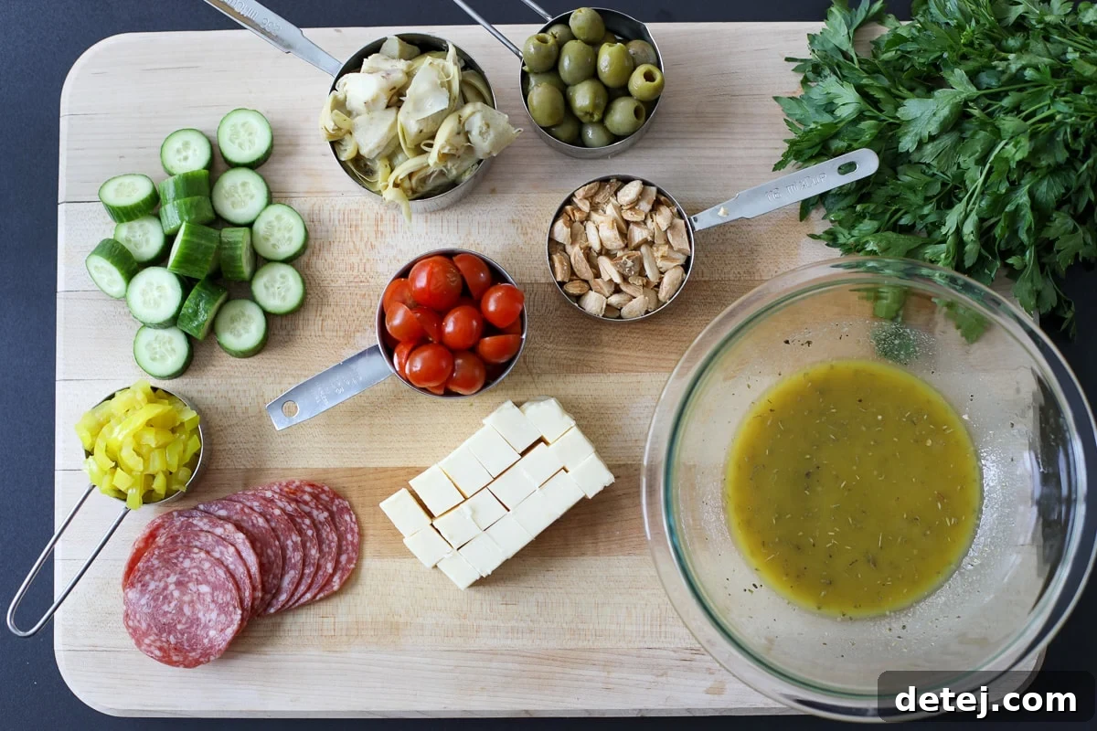 A selection of fresh ingredients including mini cucumbers, cherry tomatoes, salami, olives, artichoke hearts, and cheese, laid out for a marinated charcuterie salad.
