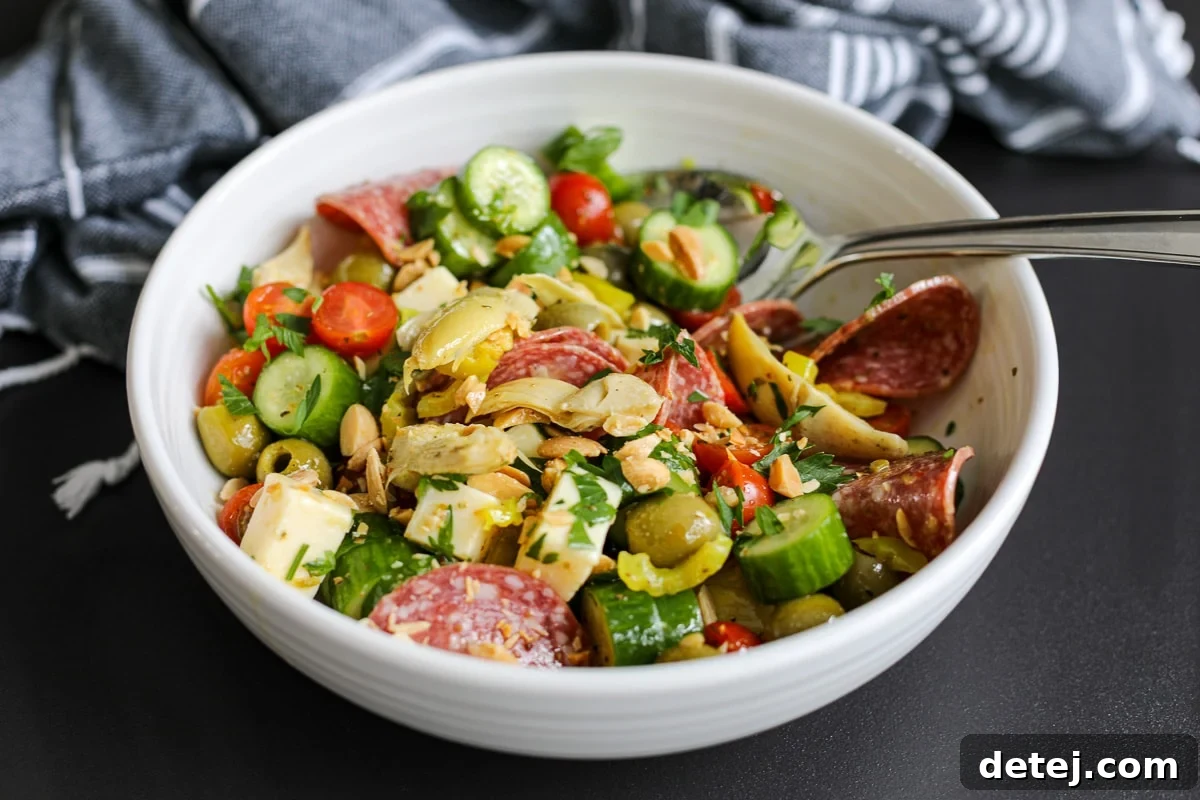 A vibrant Marinated Charcuterie Salad presented in a stylish serving bowl with a spoon, ready to be enjoyed.