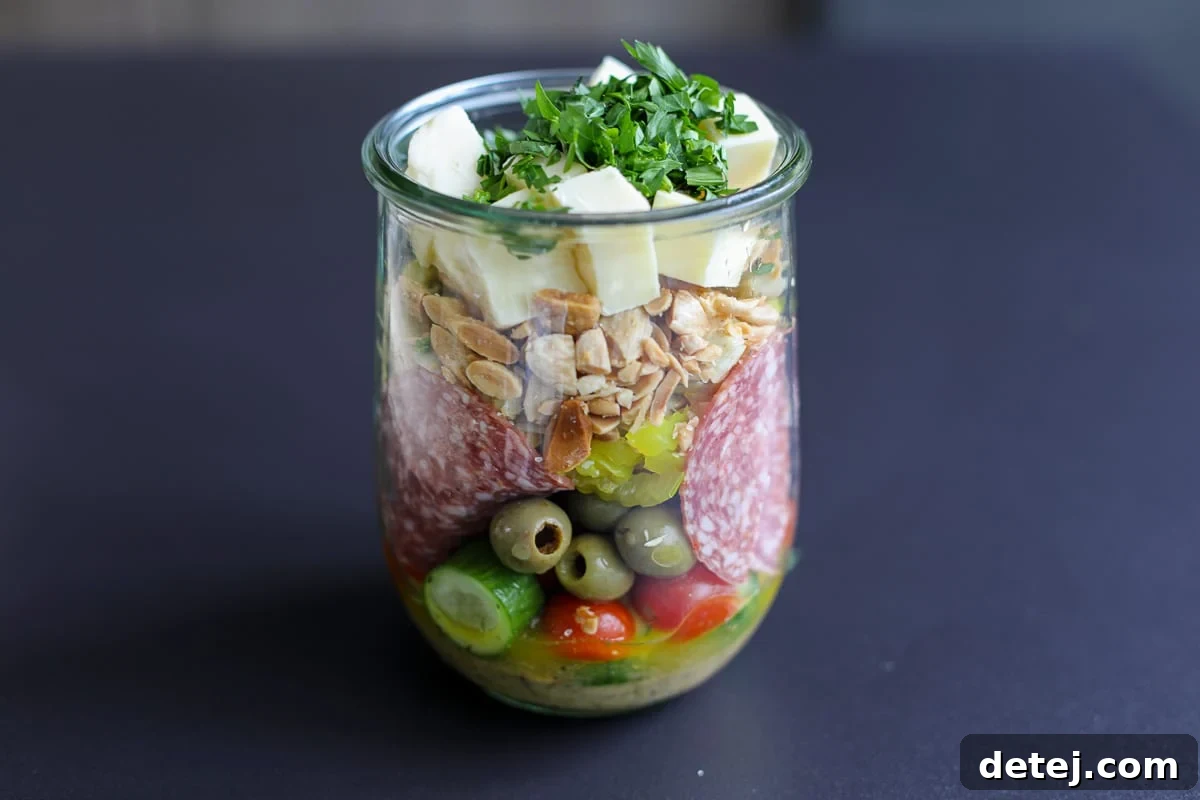 A sealed mason jar filled with a Marinated Charcuterie Salad, showing the distinct layers of ingredients before shaking.