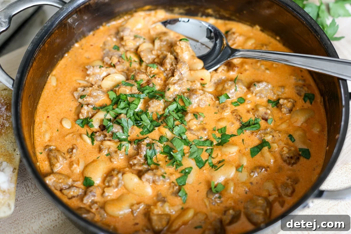 A close-up shot of the finished one-pan butter bean and sausage dip, creamy and bubbling in a skillet, topped with fresh parsley.